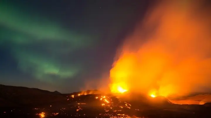 Grün leuchtende Polarlichter am Nachthimmel über einer isländischen Vulkanlandschaft, während glühende Lava und orangfarbene Rauchwolken aus einem aktiven Vulkanausbruch aufsteigen. | © Stephan Schulz