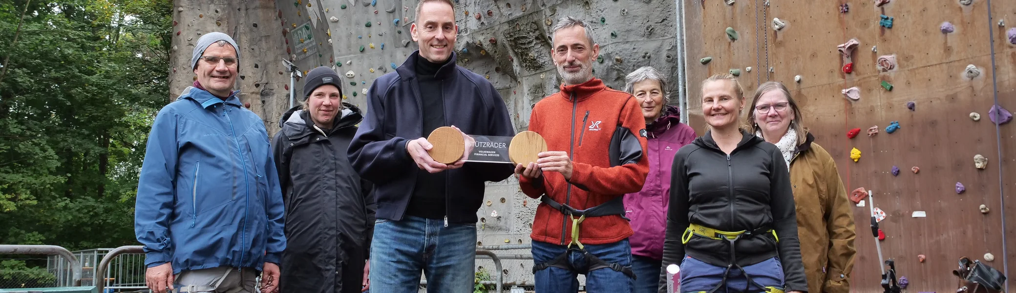Übergabe der Stützräder-Skulptur an die EWI. Von links nach rechts: Ralf Hartzsch, Ilka Töniges, Arne Puls, Stefan Burek, Christiane Podlech, Vanessa Burek und Gabriele Flammann. Im Hintergrund die Kletterwand in der Güldenstraße. | © VW Financial Services