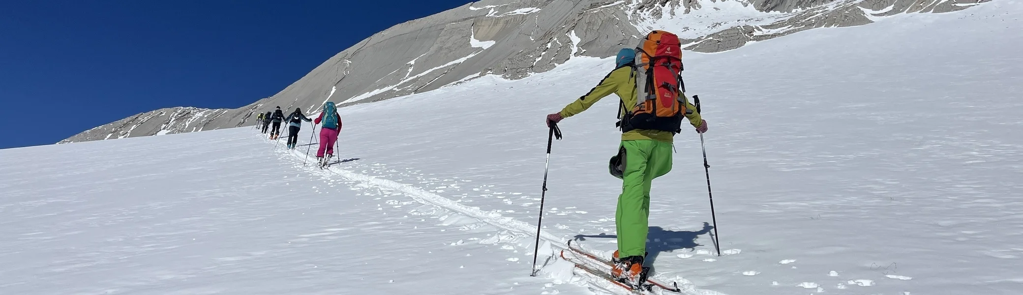 Eine Skitourengruppe im Aufstieg, fotografiert von hinten. Im Hintergrund sieht runde Felskuppen und einen wolkenlosen Himmel. | © Eva Lavon