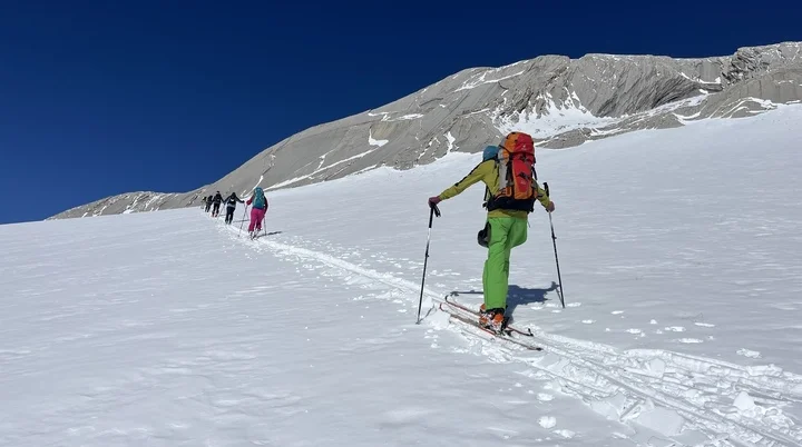 Eine Skitourengruppe im Aufstieg, fotografiert von hinten. Im Hintergrund sieht runde Felskuppen und einen wolkenlosen Himmel. | © Eva Lavon