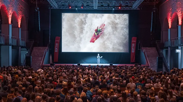 Das Bild zeigt einen dunklen Saal mit einer Leinwand. Davor sitzt eine große Audienz. | © Jana Weinert
