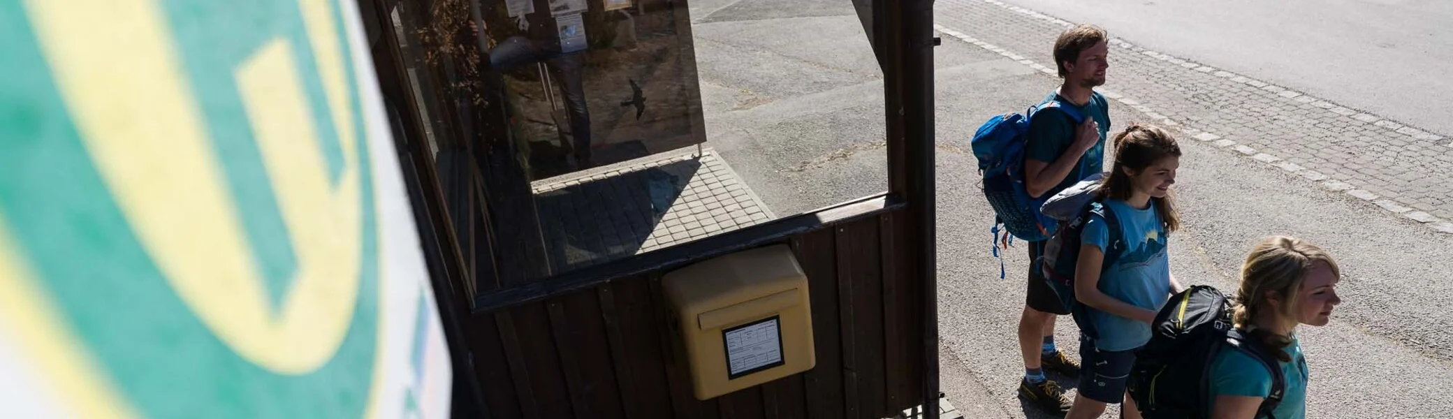 Drei Jugendliche mit Wanderrucksäcken stehen an einer Bushaltestelle | © DAV/Wolfgang Ehn