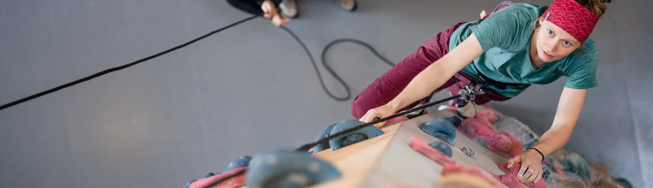 Eine Frau klettert in einer Kletterhalle, ihr Partner sichert sie. | © DAV / Julian Rohn