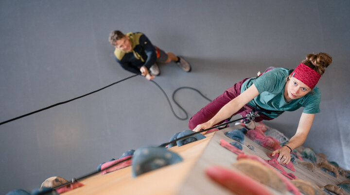 Eine Frau klettert in einer Kletterhalle, ihr Partner sichert sie. | © DAV/Marisa Koch