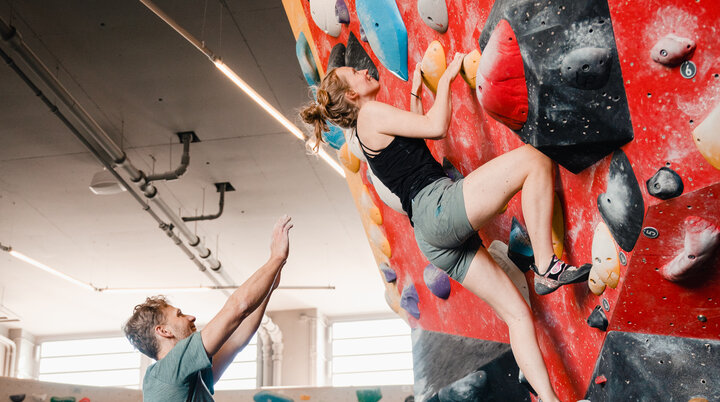 Eine Frau klettert in einer Kletterhalle, ihr Partner sichert sie. | © DAV/Marisa Koch